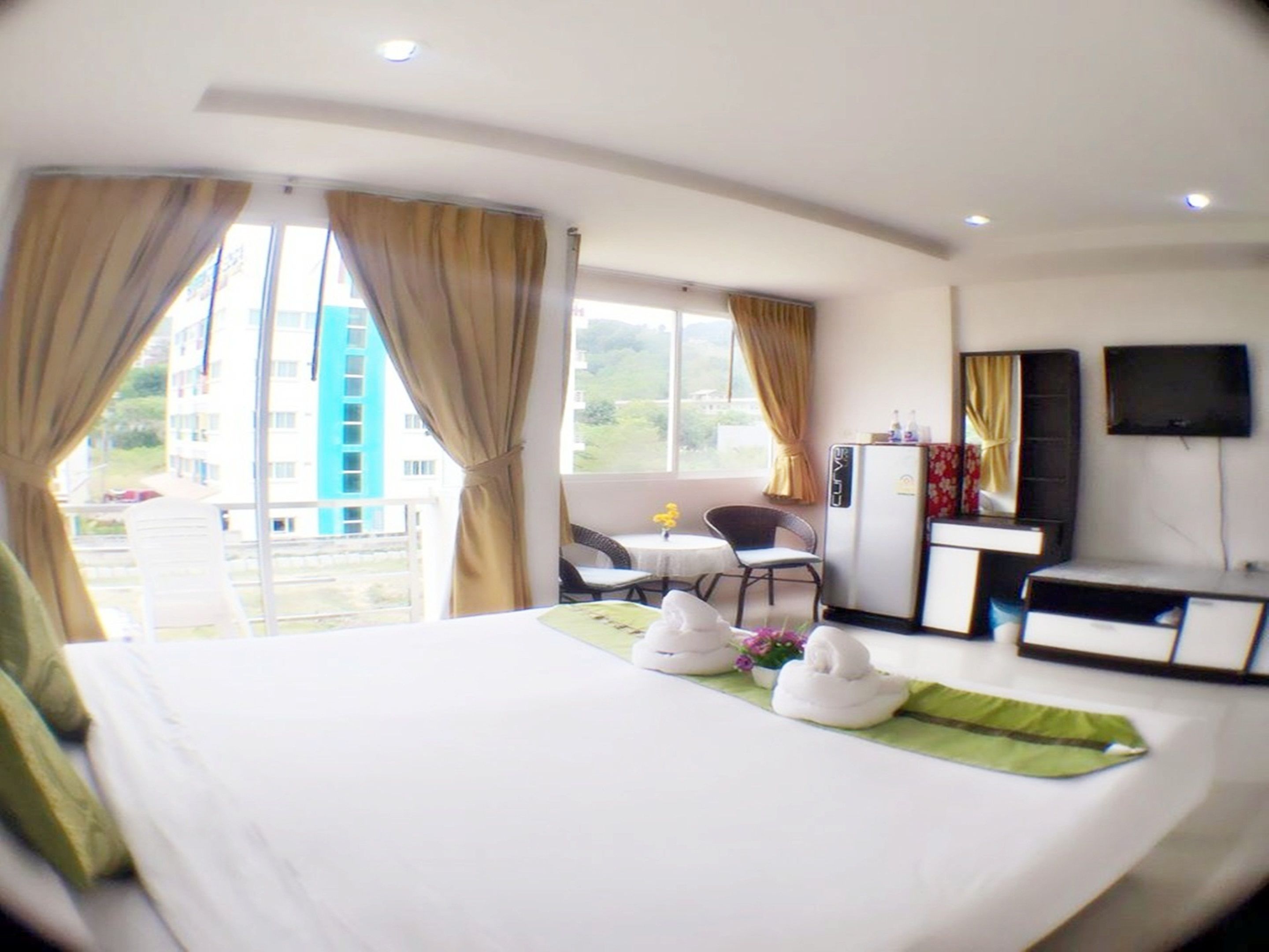 Una habitación de hotel con cama, escritorio, silla, televisión y balcón con cortinas.