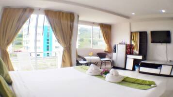 Una habitación de hotel con cama, escritorio, silla, televisión y balcón con cortinas.