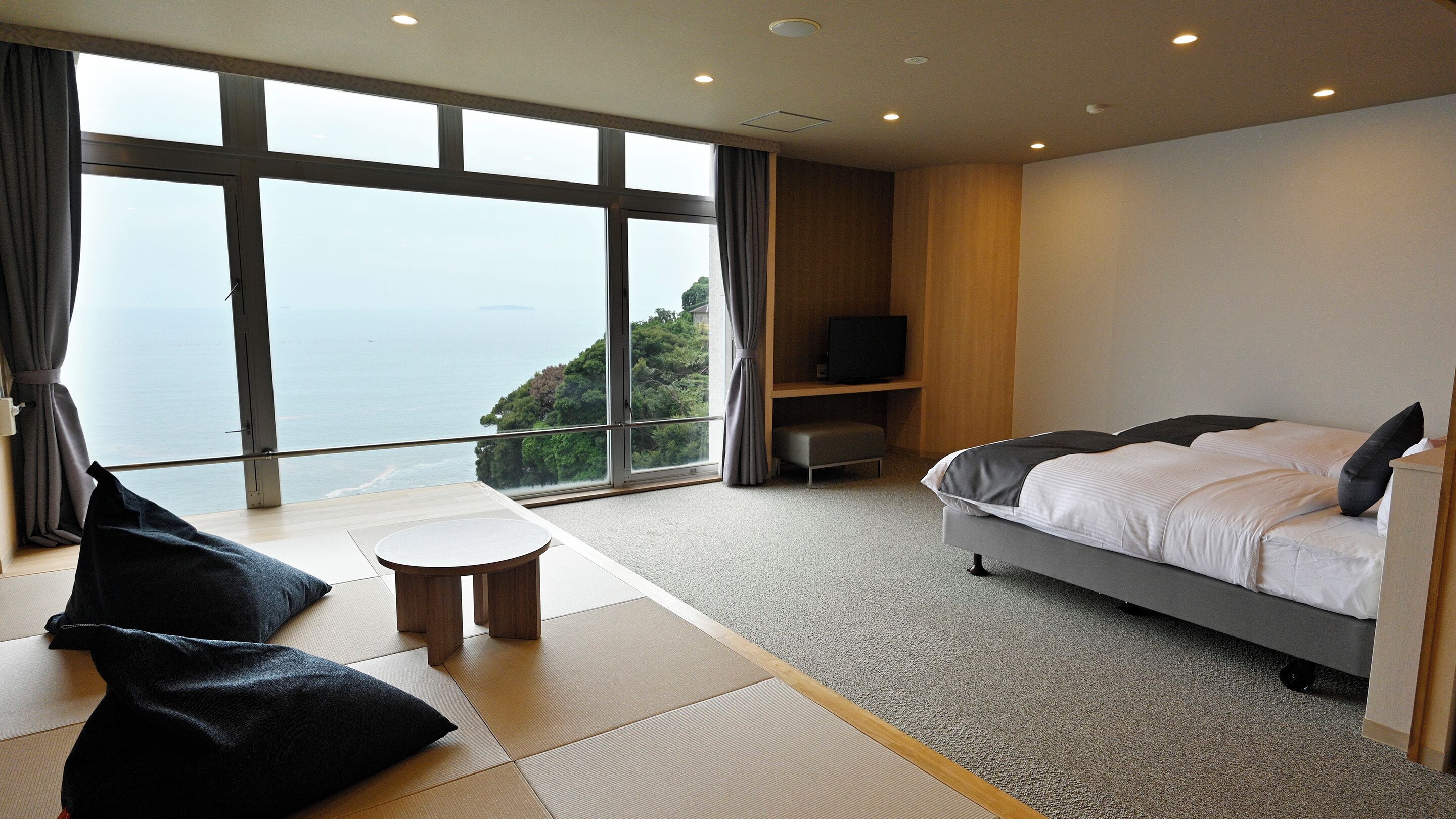 A hotel room with a large window, a bed, a small table, and a TV.