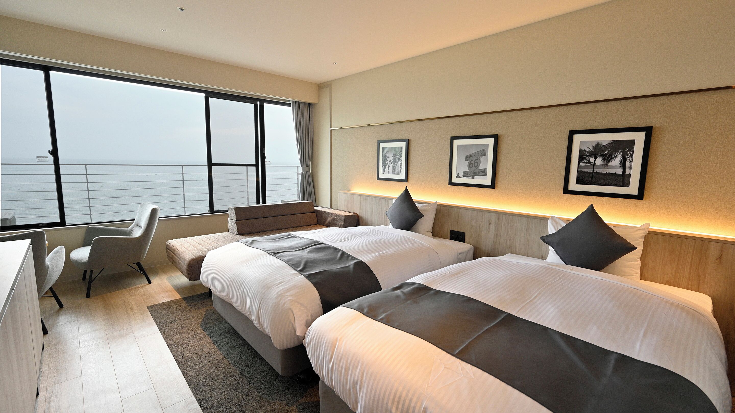 A hotel room with two beds, a desk, and a view of the sea.