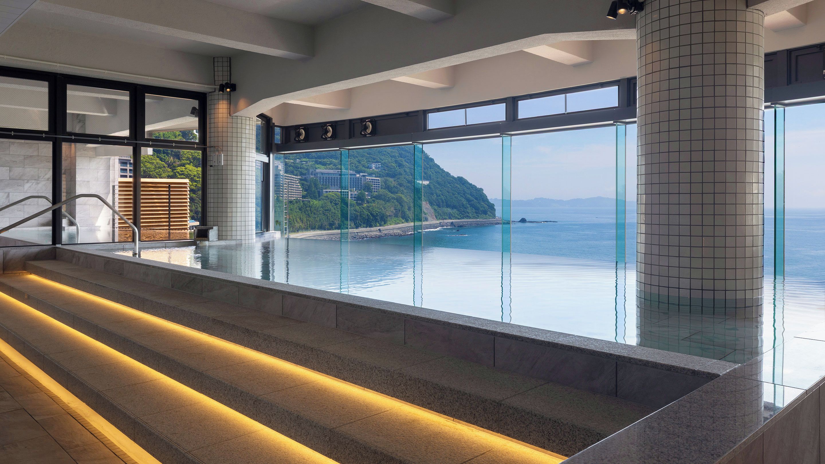 A modern indoor swimming pool with a view of a coastal landscape.