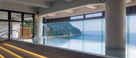 A modern indoor swimming pool with a view of a coastal landscape.