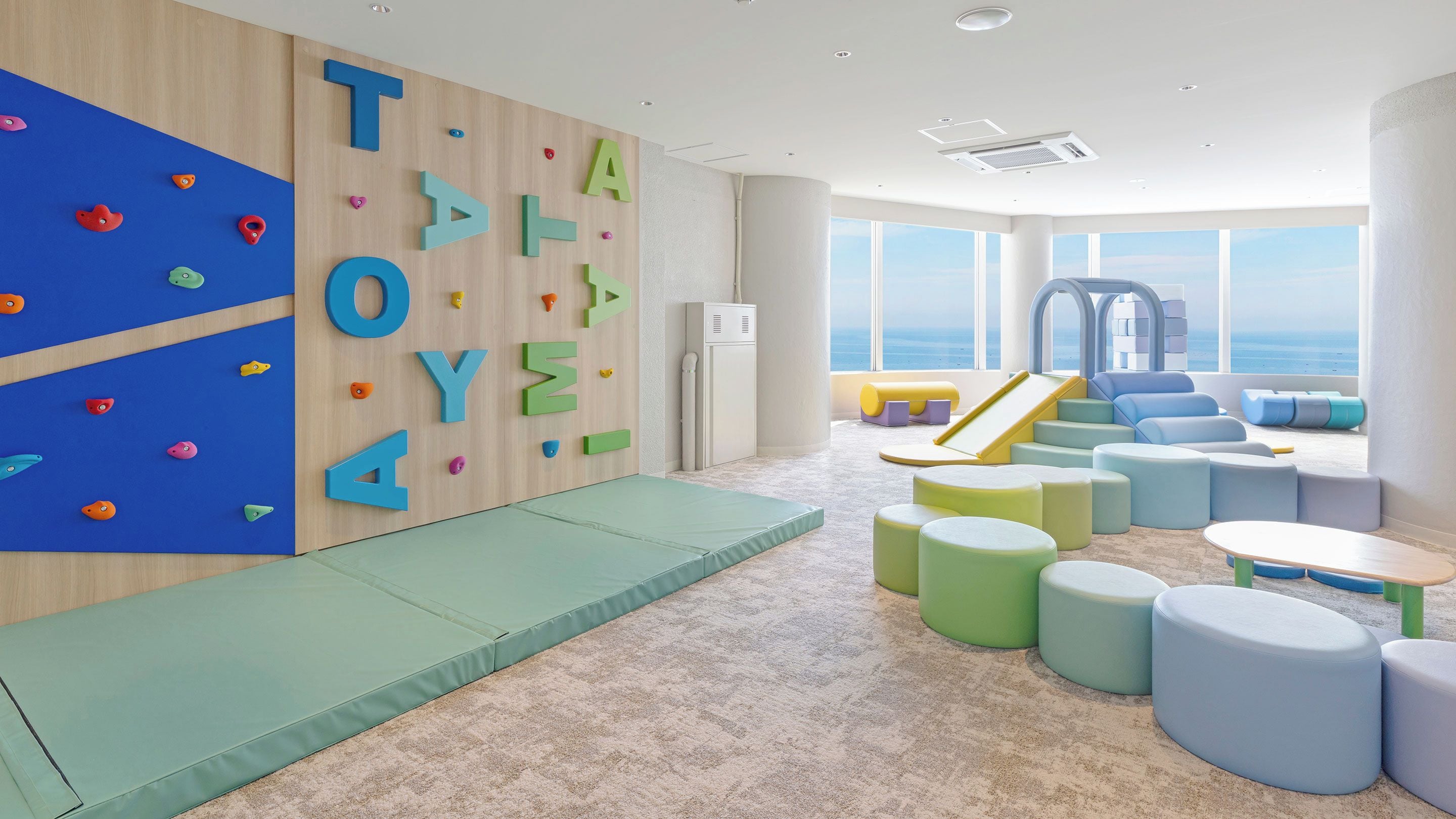 A children's playroom with climbing walls, soft seating, and a slide.