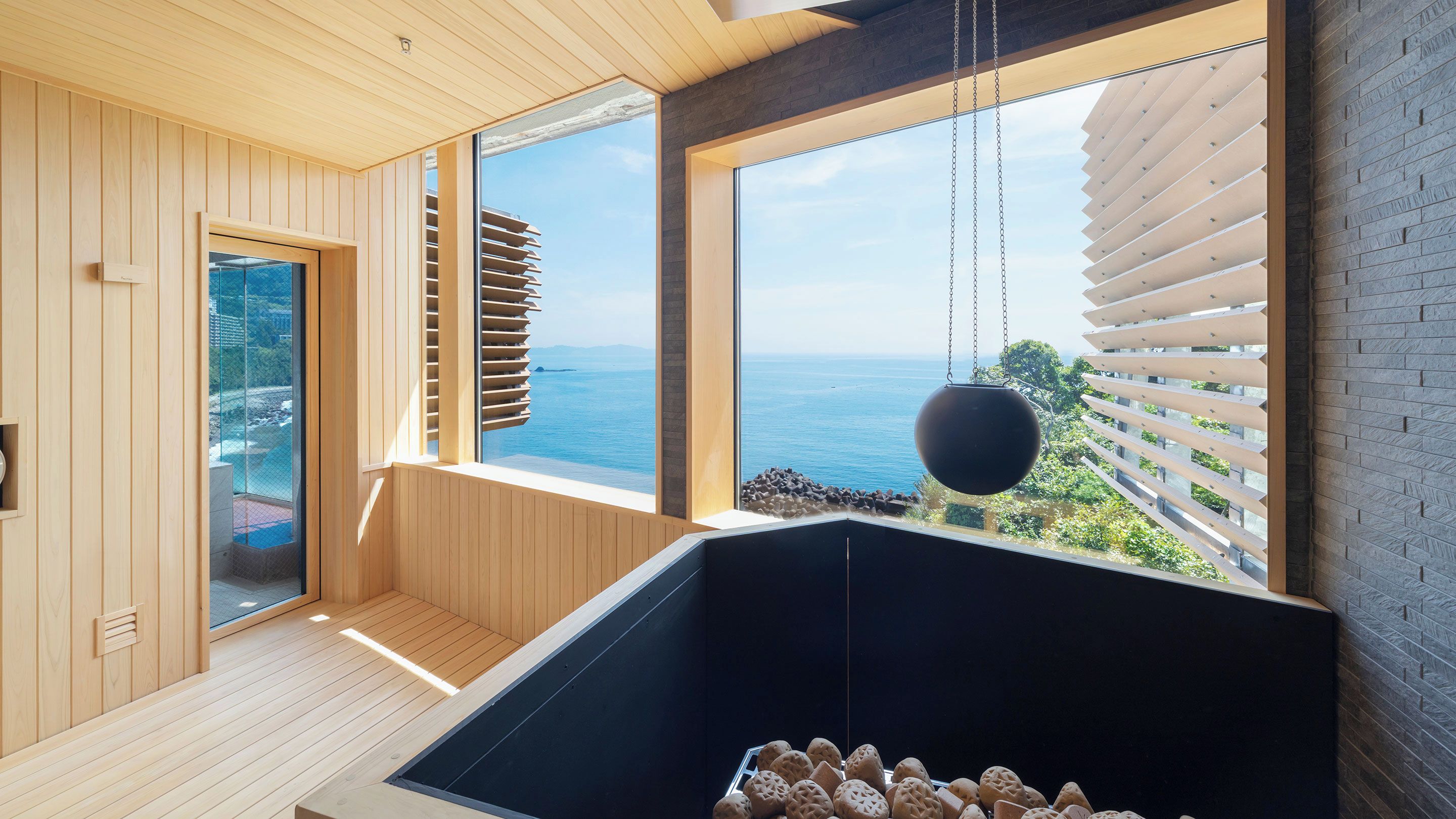 A modern interior with wooden paneling, a black heated floor, and large windows overlooking the sea.