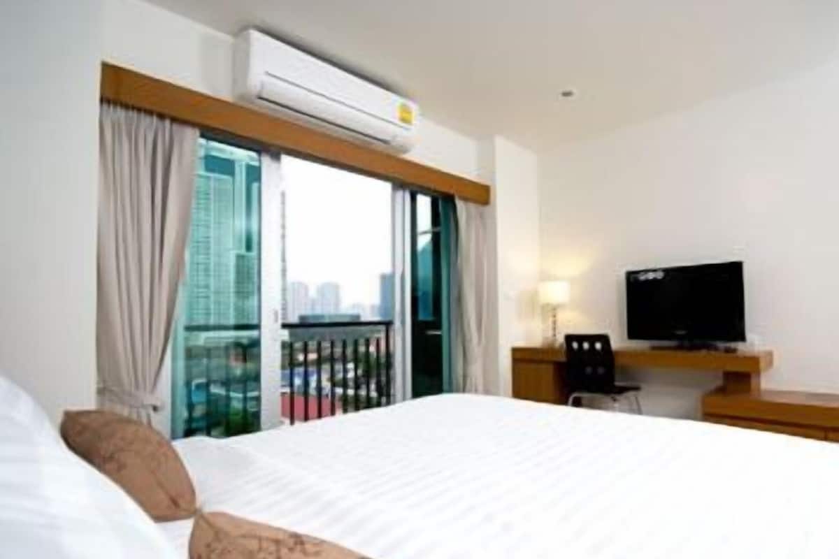 A hotel room with a bed, a TV, and a window with curtains.