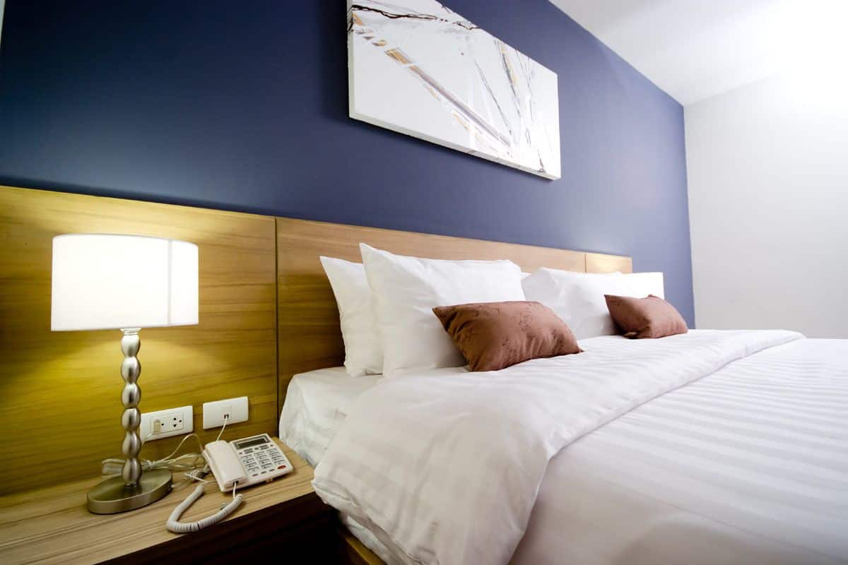 A hotel room with a bed, a bedside lamp, a phone, and a wall-mounted artwork.