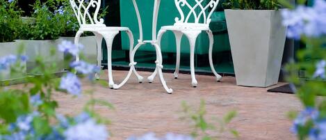 A patio area with a white metal table and two chairs, surrounded by potted plants and flowers.