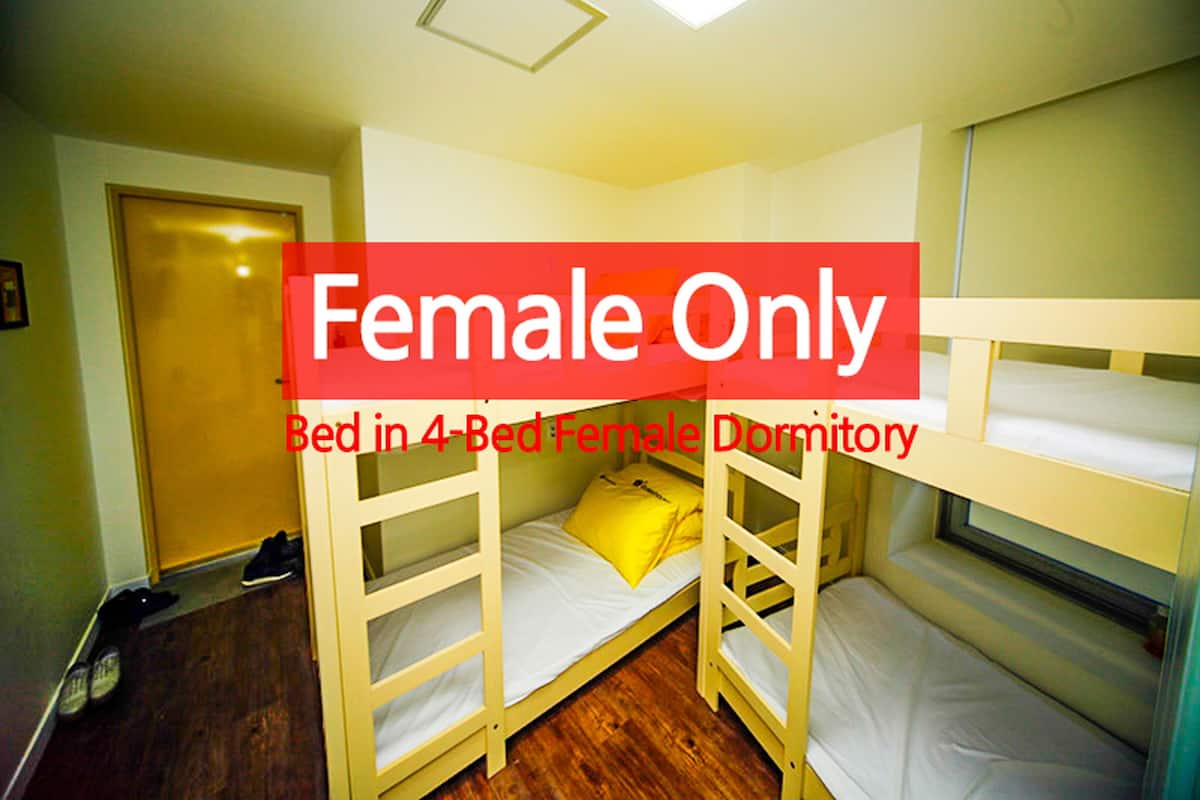 Ein 4-Bett-Schlafsaal mit Etagenbetten, einer Tür und einem Paar Schuhe auf dem Boden.