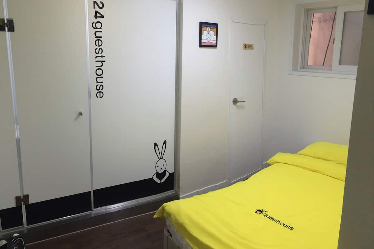Ein Zimmer mit einem Bett, einer Tür mit der Aufschrift "24 Guesthouse" und einem kleinen Fenster.