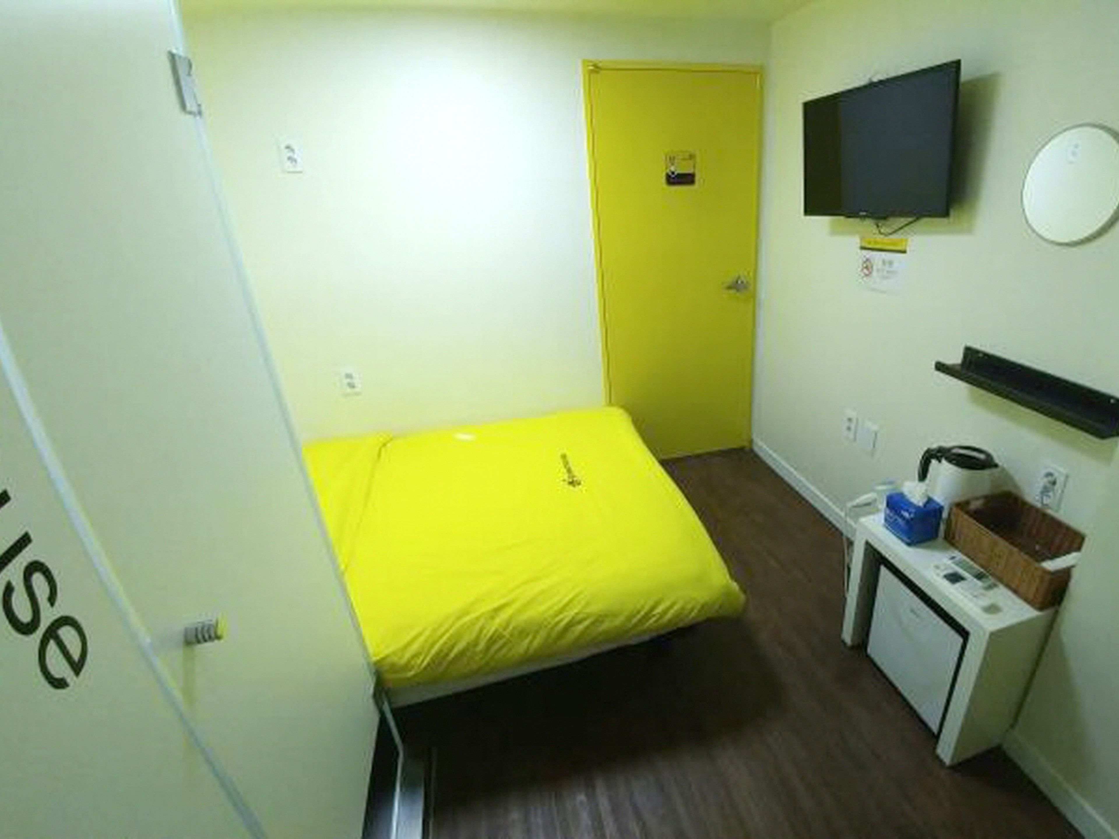 A small room with a bed, a television, a desk with a computer, and a washing machine.