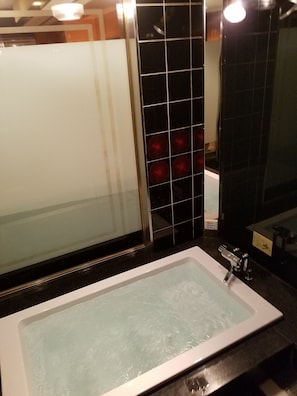 Un baño con una bañera rectangular, cabina de ducha con mampara de vidrio y pared cubierta de baldosas negras.