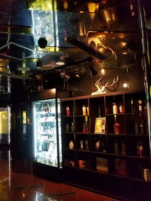 Un interior moderno con una vitrina de vidrio llena de diversos objetos, estantes con botellas y una pieza decorativa de asta en la pared.