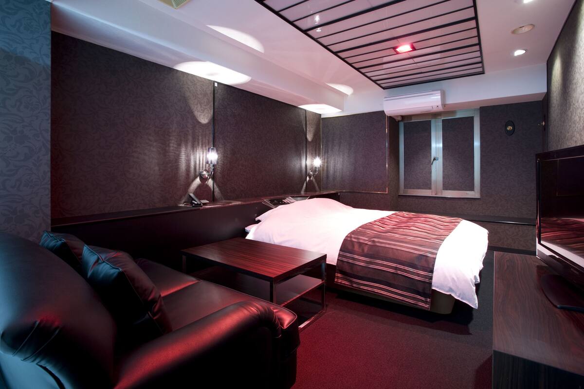 A hotel room with a bed, a sofa, a TV, and a desk.