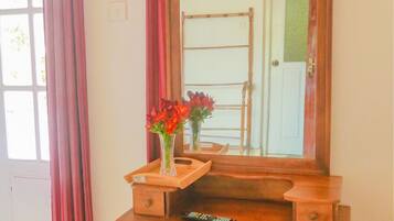 Un tocador de madera con espejo, un jarrón con flores y un control remoto encima.