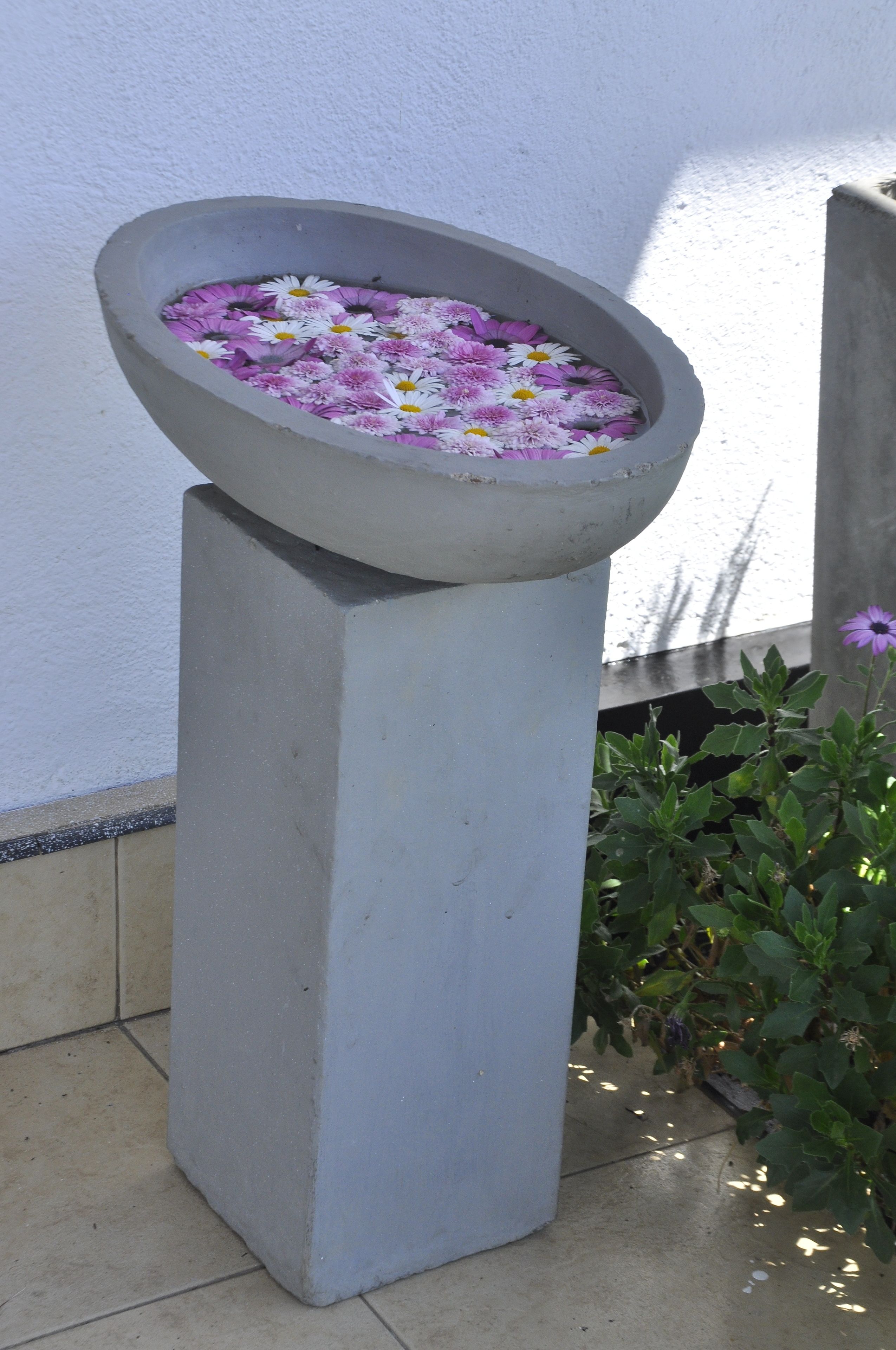 Macetas de hormigón con agua y flores sobre un suelo de baldosas.