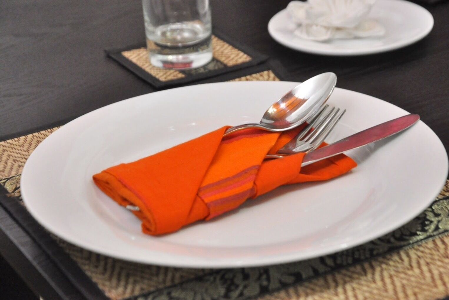 Un plato blanco con una servilleta naranja doblada y cubiertos sobre una mesa.