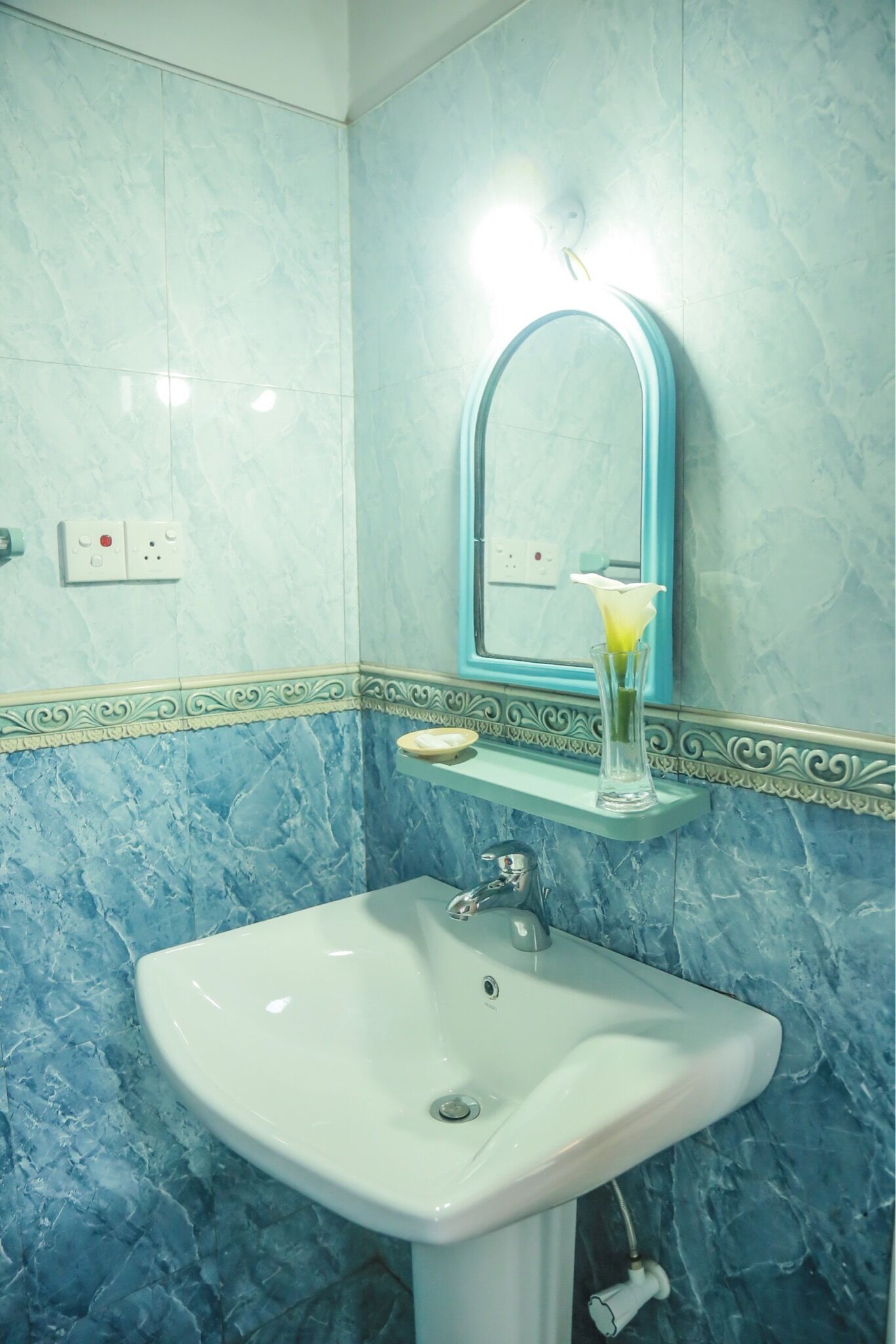 Une salle de bain avec un lavabo blanc, un miroir et un vase de fleurs.