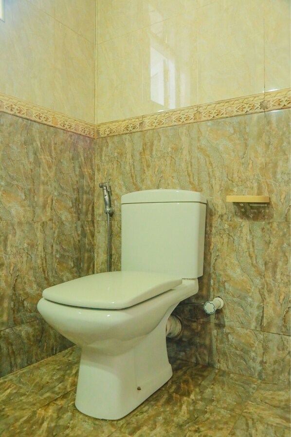 Une salle de bain avec des toilettes blanches, des murs en marbre et un espace douche.