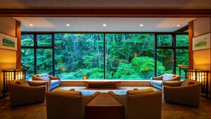 Habitación con un gran ventanal que ofrece vistas al bosque, un conjunto de sofás y una mesa de madera.