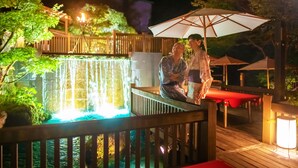Una pareja sentada en una terraza de madera, cerca de una cascada y una mesa roja.