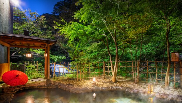 Un onsen japonés tradicional con un pabellón de madera, una fuente termal de piedra y un paraguas rojo.