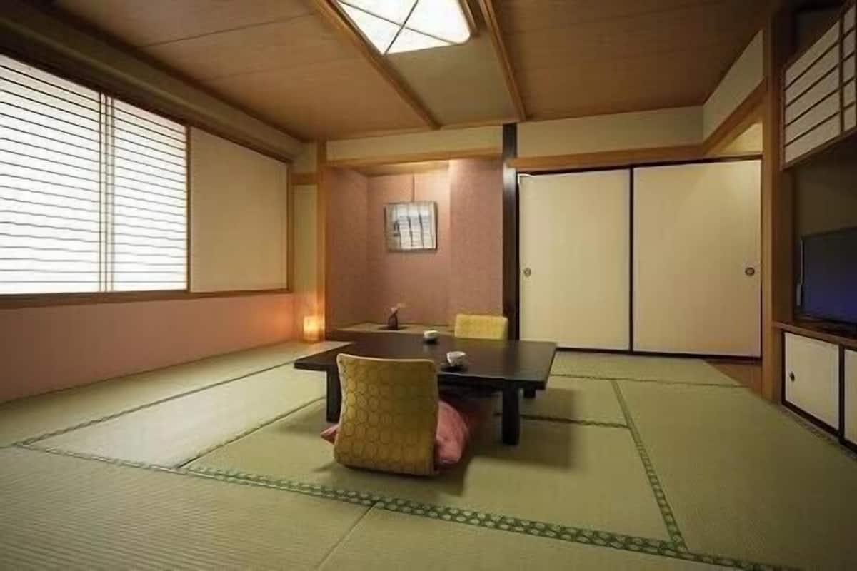 A traditional Japanese room with tatami flooring, a low table, a television, and sliding doors.