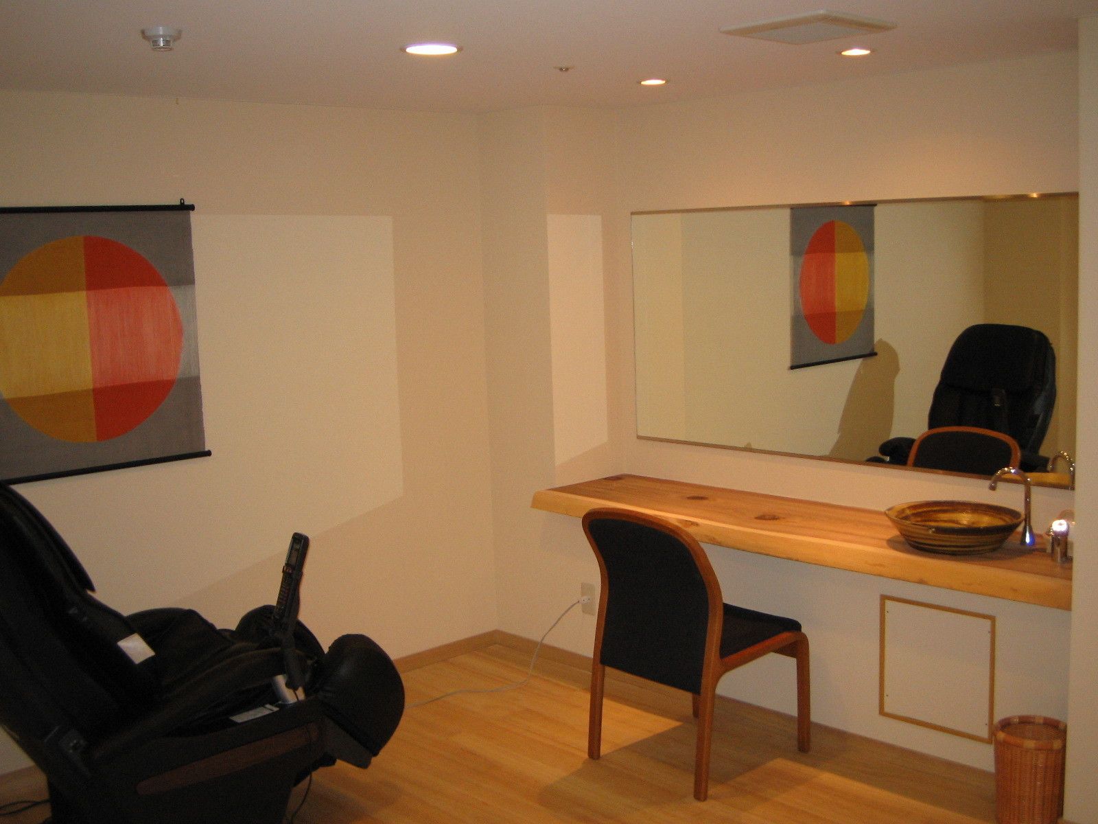 A room with a wooden desk, a chair, a guitar, a mirror, and a wall with a geometric painting.