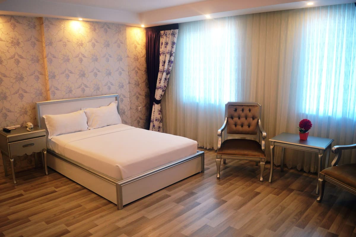A hotel room with a large bed, a chair, a small table, and a nightstand.
