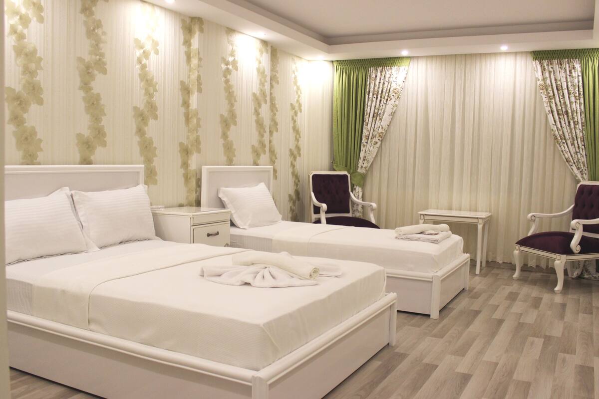 A hotel room with two beds, a chair, a small table, and a nightstand.