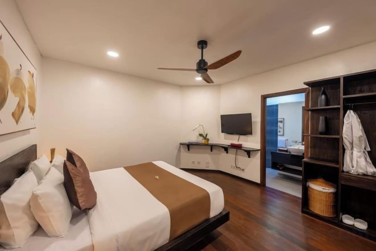 A modern bedroom with a bed, a ceiling fan, a TV, a desk, and a wardrobe.