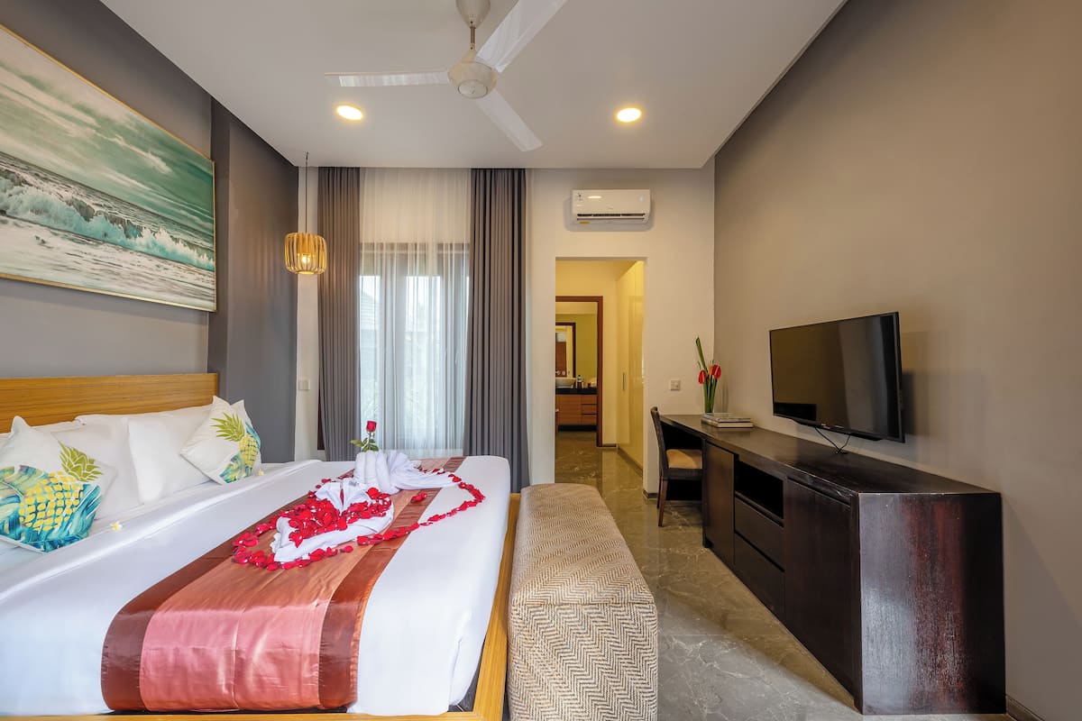 A hotel room with a bed, a desk, a television, and an air conditioning unit.