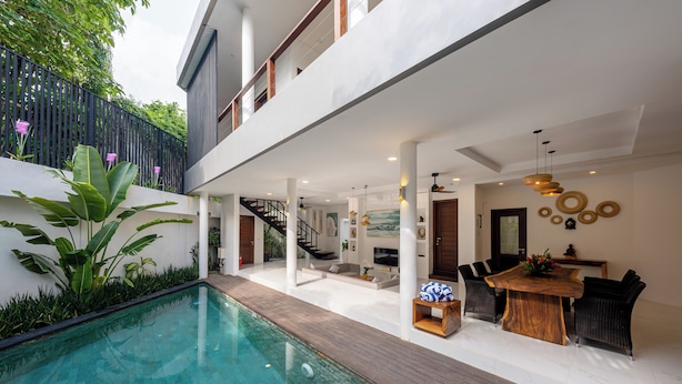 Un espacio exterior moderno con piscina, terraza de madera y comedor con mesa y sillas de madera.