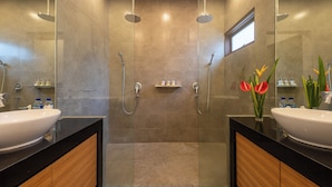 Un baño moderno con dos lavamanos, zona de ducha con mampara de vidrio y un ventanal pequeño.