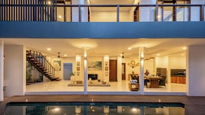 Una casa moderna de dos pisos con un amplio salón envuelto en vidrio, una escalera y una piscina.