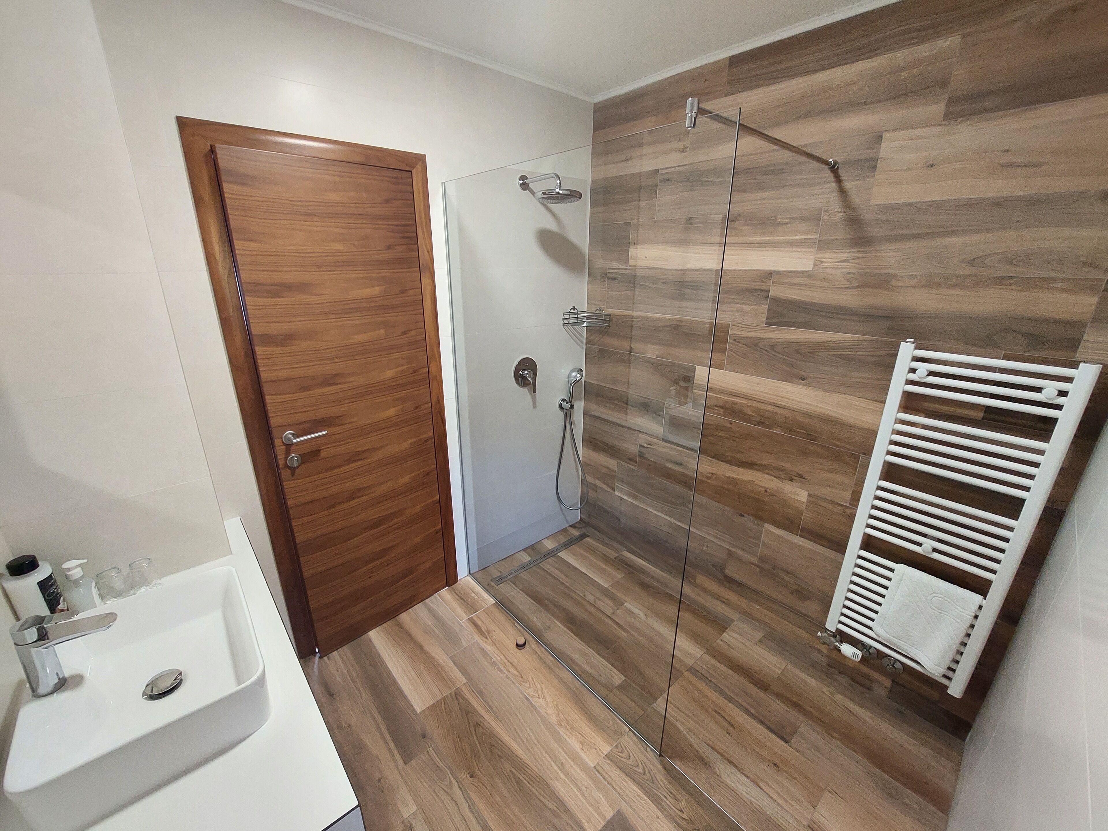 A bathroom with a wooden door, a shower with a glass enclosure, and a white towel rack.