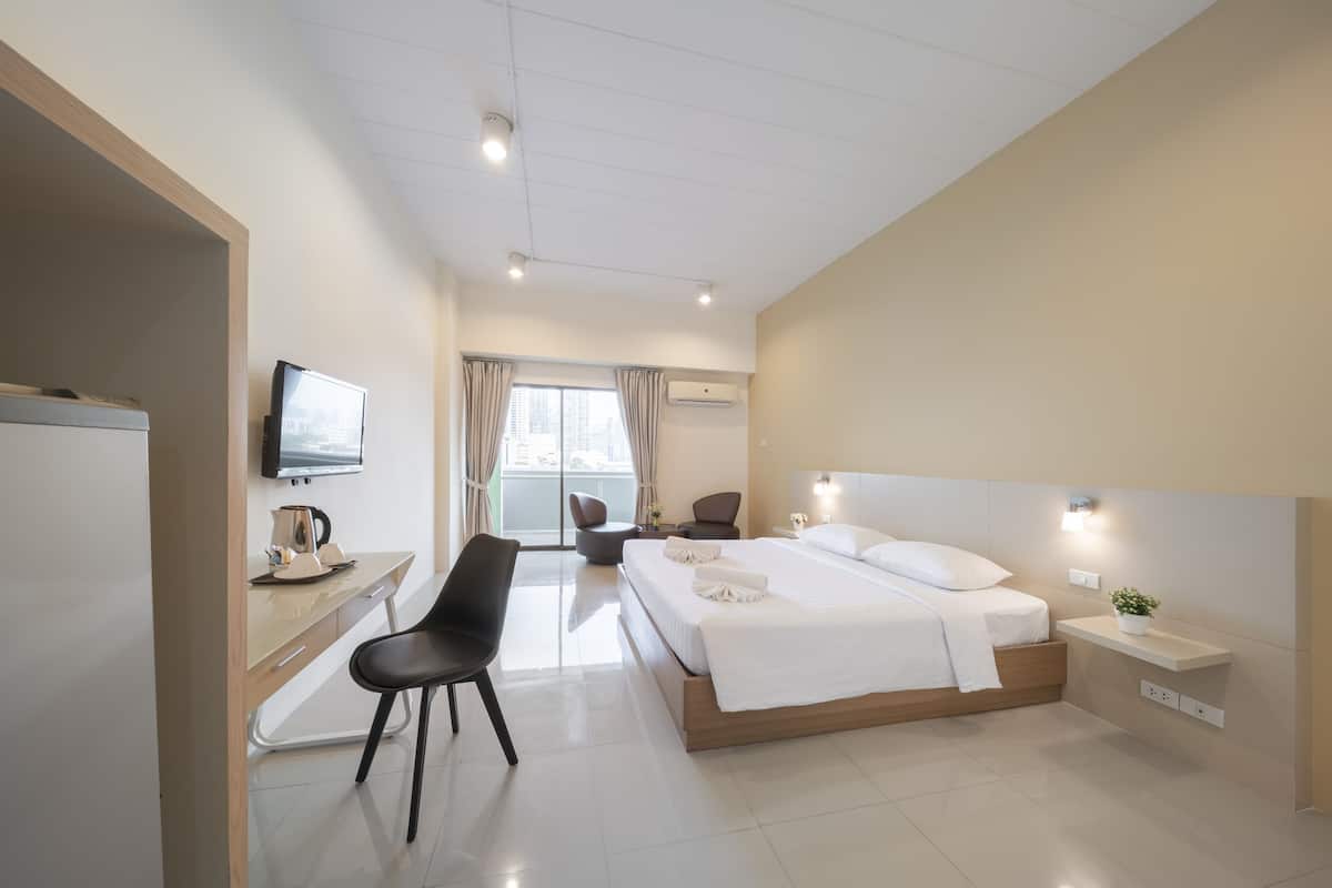 A modern hotel room with a bed, desk, chair, TV, and a small plant.