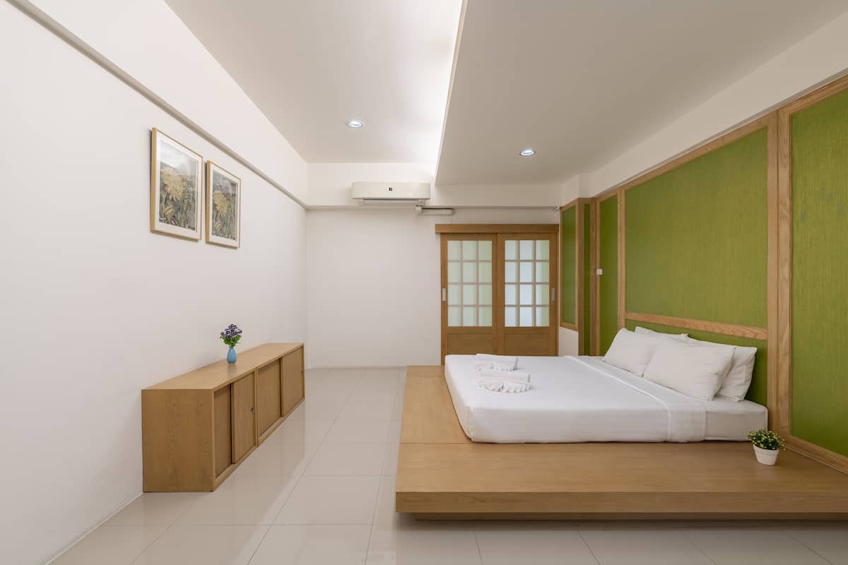 A modern bedroom with a wooden bed, a small bedside table, a wall-mounted air conditioner, and a green accent wall.