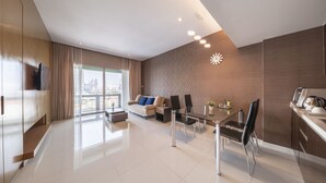 Un salon moderne comprenant un canapé, une table à manger et des chaises, un téléviseur, et offrant une vue sur la ville grâce à de grandes fenêtres.