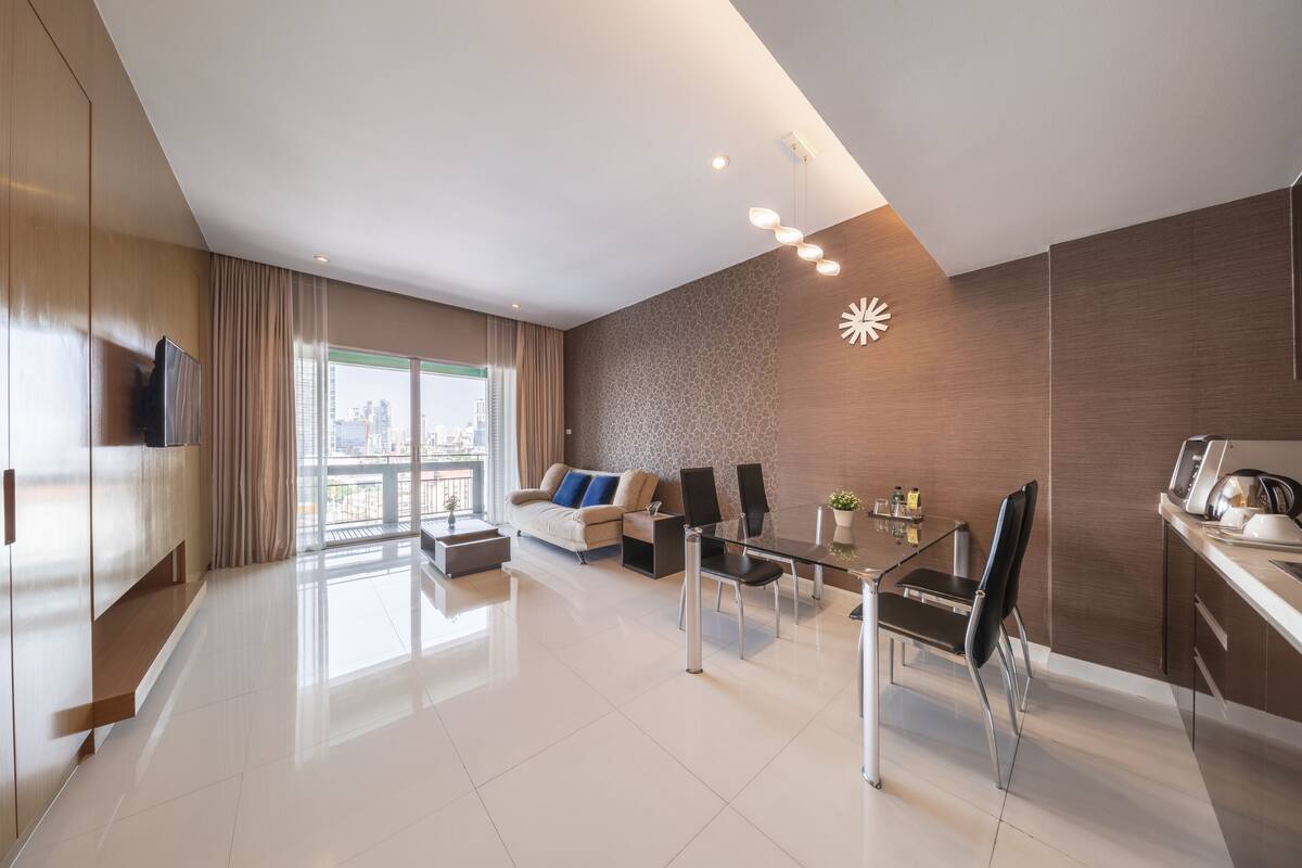 A modern living room with a sofa, dining table, and chairs, a TV, and a city view through large windows.
