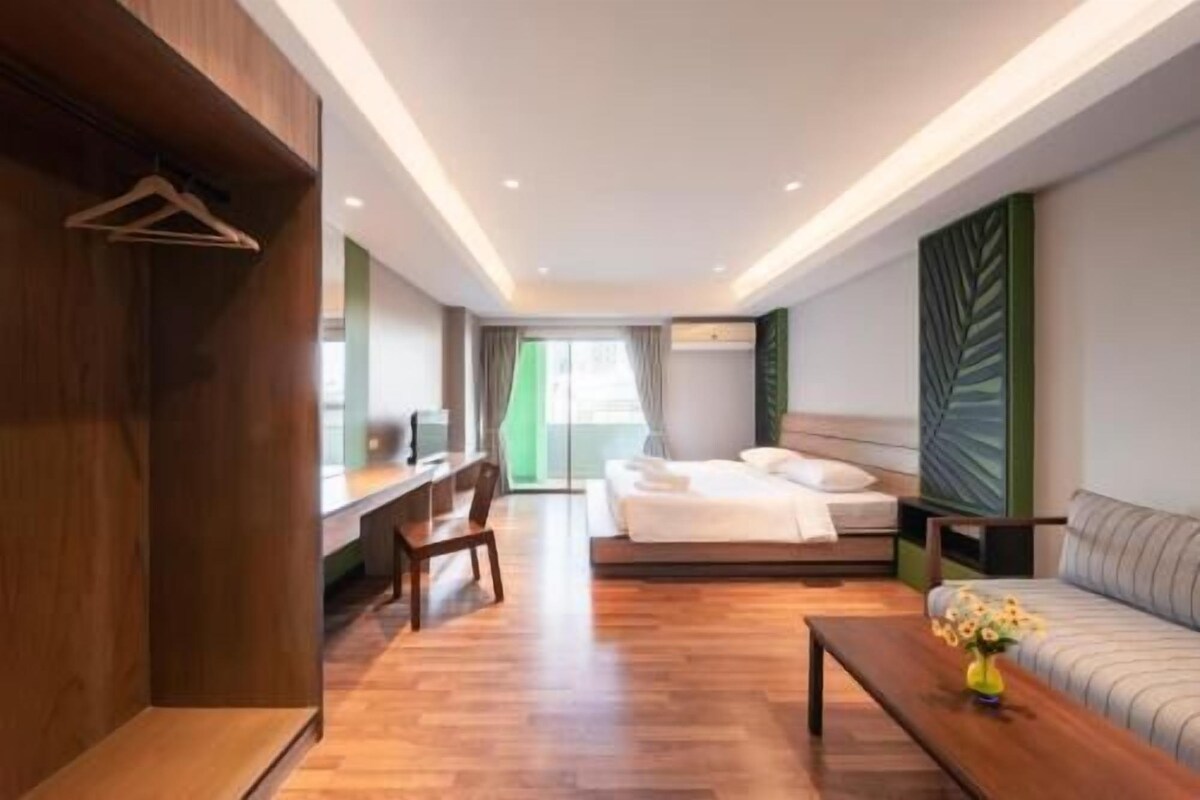 A modern hotel room with a bed, a desk, a chair, a sofa, and a coffee table.