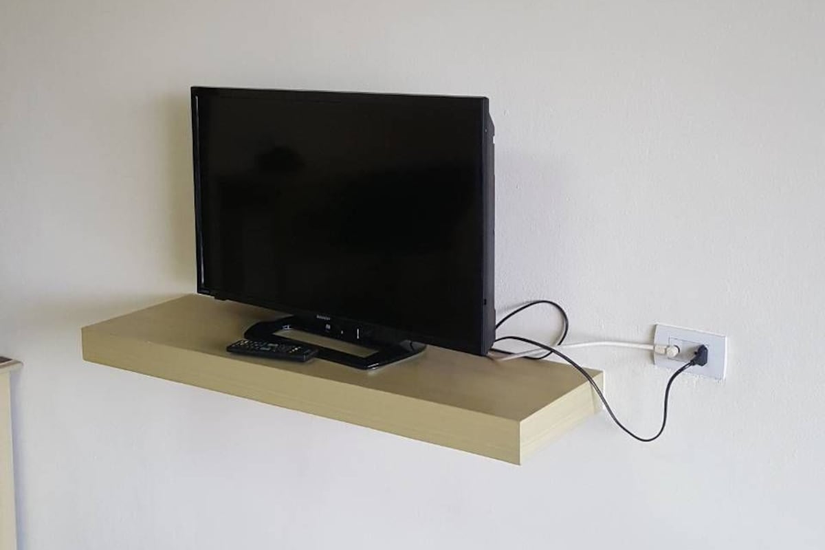 A television mounted on a wall with a remote control and power cable.
