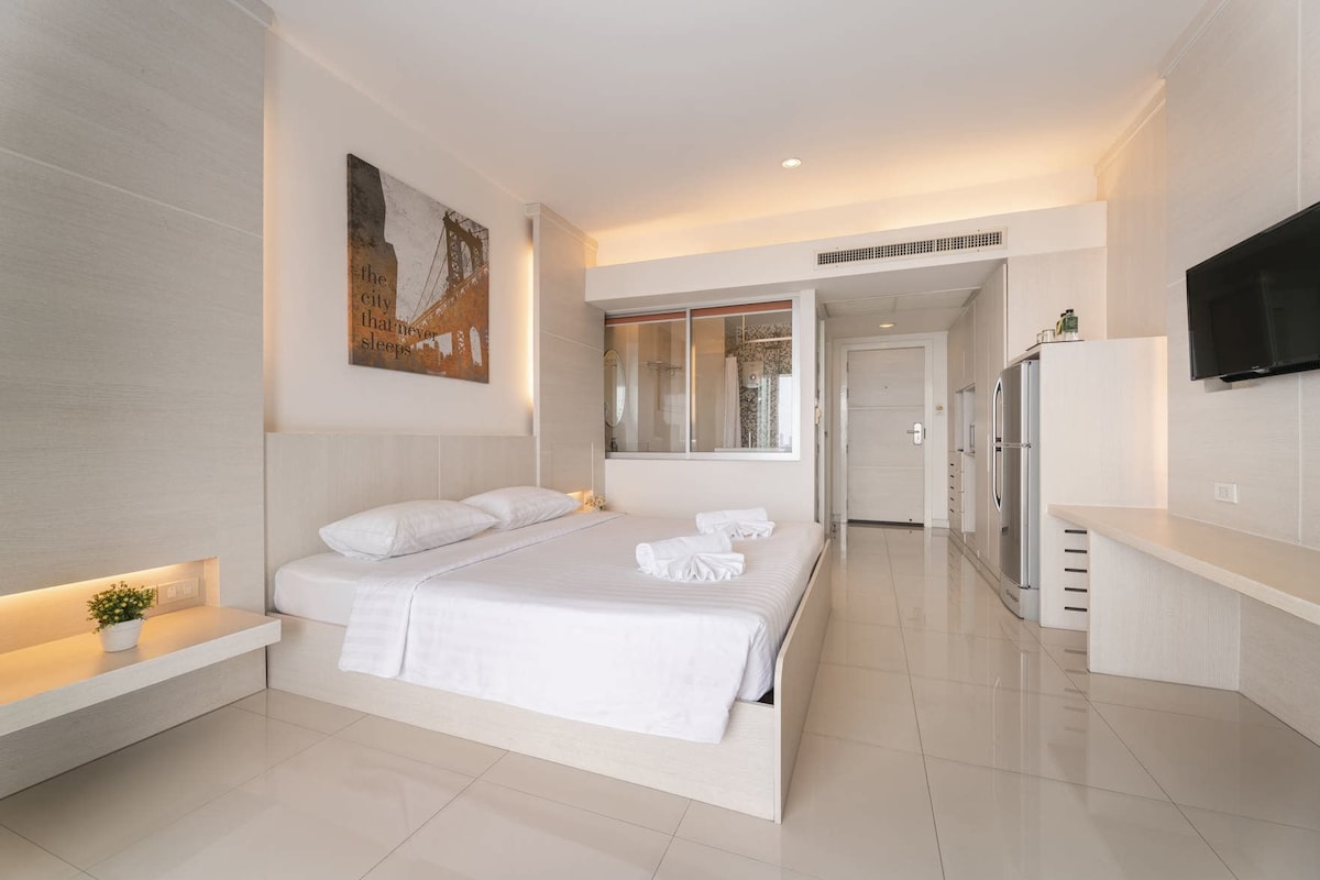 A modern hotel room with a large bed, a flat-screen TV, and a bathroom visible through a glass door.