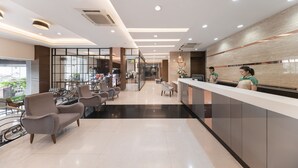 Un hall d’hôtel moderne doté d’un comptoir d’accueil, d’un espace salon et offrant une vue sur l’extérieur.