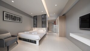 Une chambre moderne comprenant un lit, une chaise, un téléviseur et un couloir menant à la cuisine.