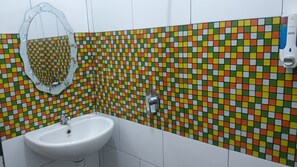 Ein Badezimmer mit einem weißen Waschbecken, einem Spiegel und einer gefliesten Wand mit einem farbenfrohen Mosaikmuster.