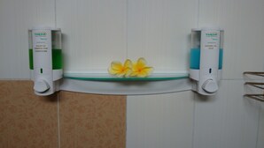 A bathroom with a glass shelf holding a yellow flower, flanked by two THEDA shampoo and conditioner dispensers.