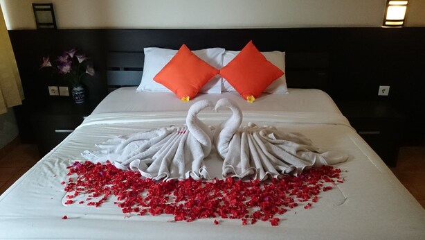 A bed with a swan towel arrangement and rose petals.