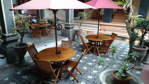 An outdoor seating area with wooden tables and chairs, surrounded by potted plants and umbrellas.
