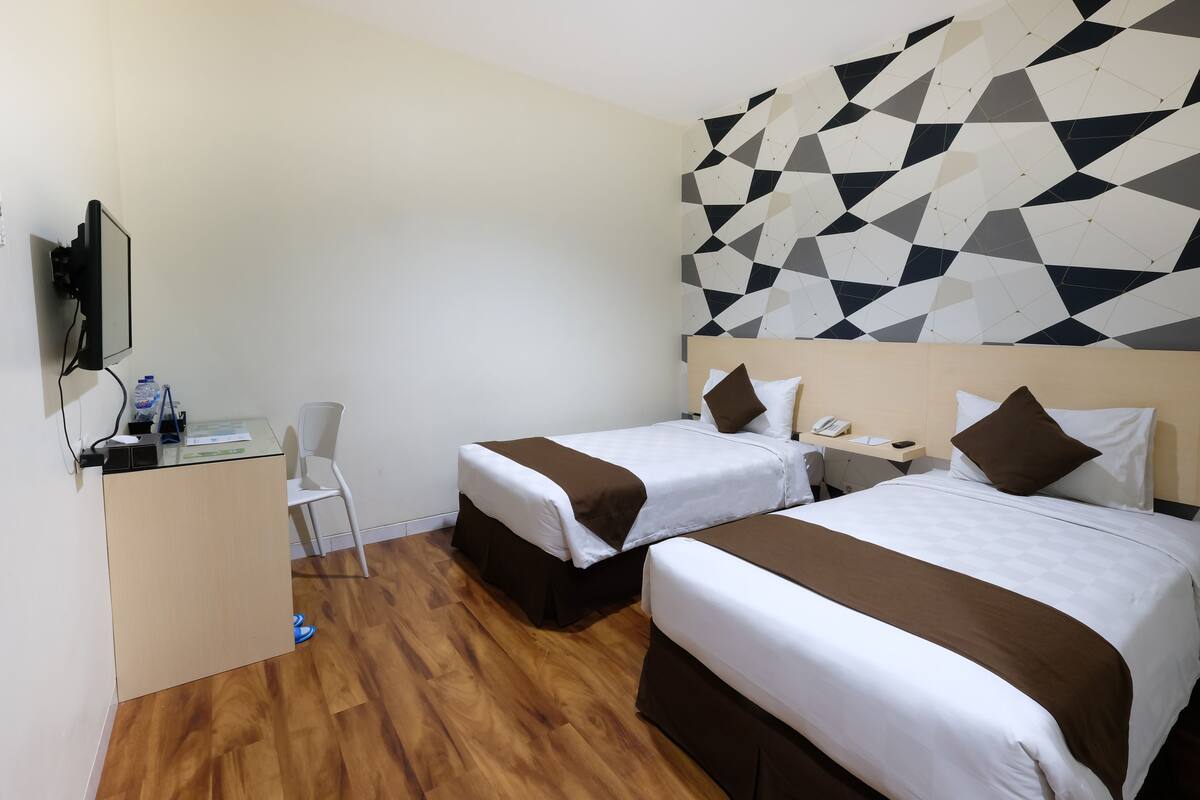 Une chambre d’hôtel avec deux lits, un bureau, une chaise et un mur orné d’un motif géométrique.