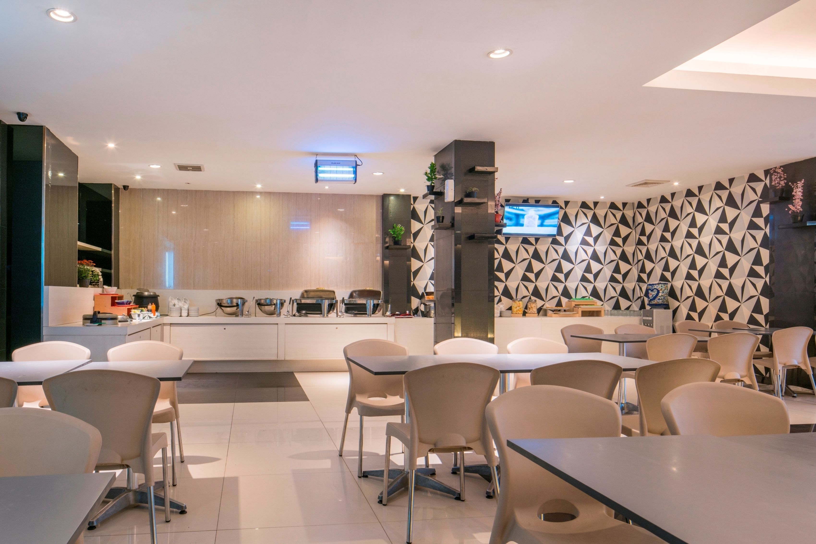 A modern dining area with tables and chairs, a kitchen counter, and a patterned wall.